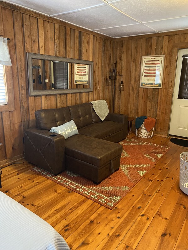 Una sala de estar acogedora con un sofá seccional de cuero marrón, un tapete estampado y paredes de madera.