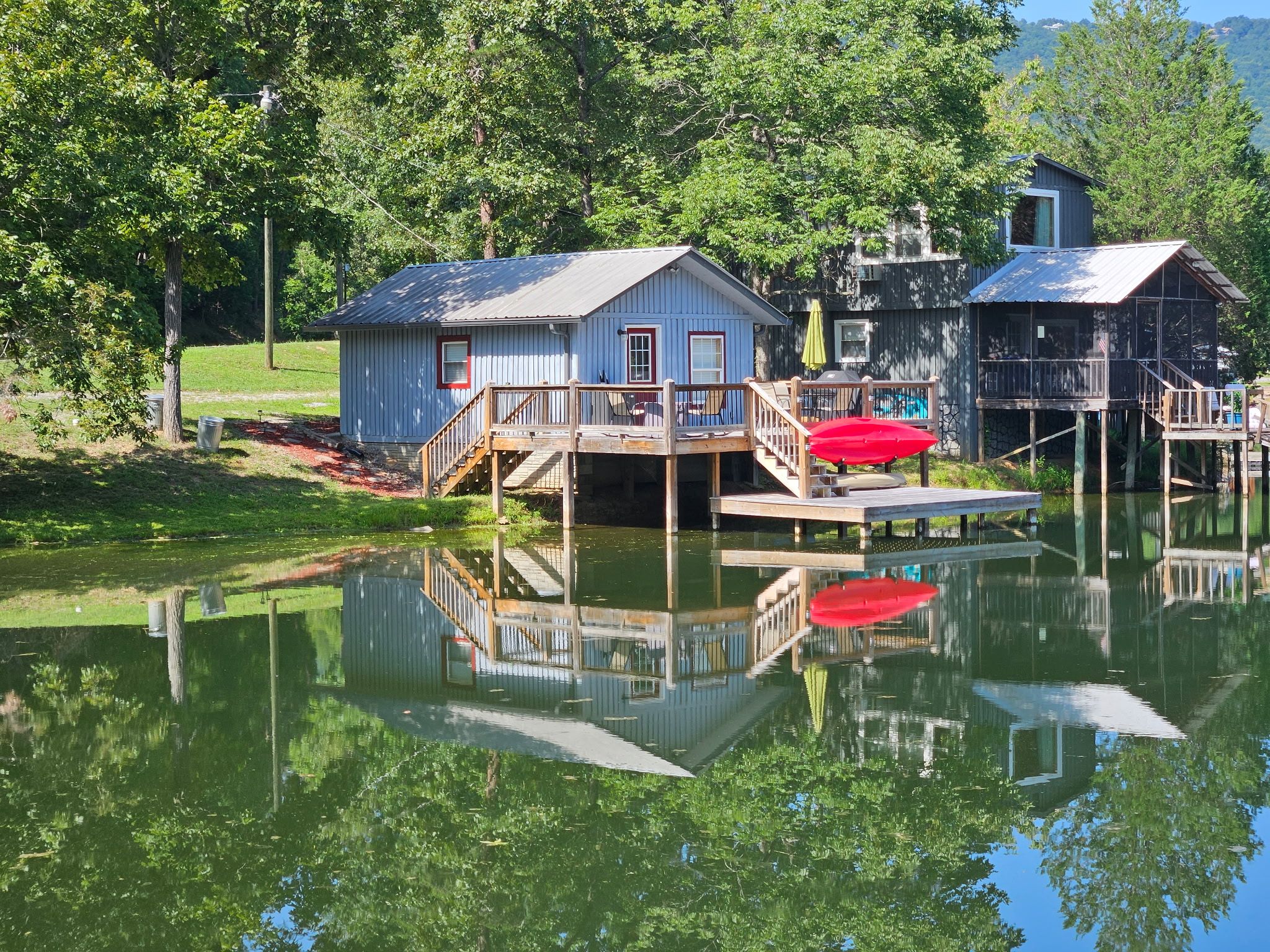 A lakeside cabin with a dock, a red umbrella, and a small boat.