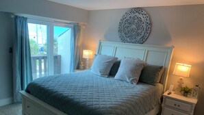 A bedroom with a bed, two bedside tables, a nightstand, a decorative wall piece, and a view through a window. - Sea Esta Getaway - Largo Mar (Panama City Beach)