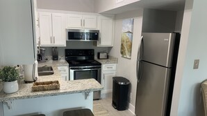 A modern kitchen with white cabinets, stainless steel appliances, granite countertops, and a small island with stools. - Sea Esta Getaway - Largo Mar (Panama City Beach)