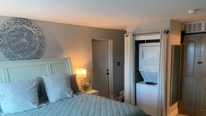 A bedroom with a bed, a nightstand, a lamp, a wardrobe, and a washing machine. - Sea Esta Getaway - Largo Mar (Panama City Beach)