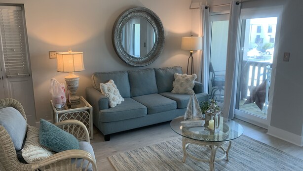 A living room with a grey sofa, wicker chairs, a glass coffee table, and a large mirror on the wall. - Sea Esta Getaway - Largo Mar (Panama City Beach)
