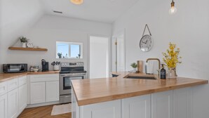 Cocina moderna con armarios blancos, encimera de madera, electrodomésticos de acero inoxidable y una lámpara colgante.