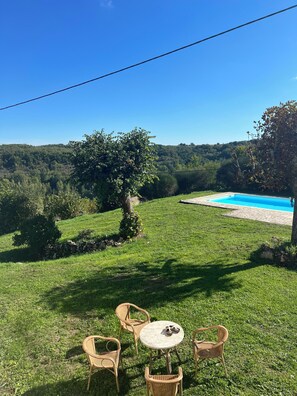 Un espacio al aire libre con césped, una piscina, mobiliario de mimbre y vistas a una ladera boscosa.