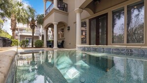 A swimming pool with clear water, surrounded by a building with columns and a balcony. - Suzie Q, Luxury Beach House w/Private Pool Rooftop Deck (Destin)