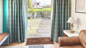 Una habitación con vista a un sendero de piedra que lleva a una casa, un banco y una lámpara sobre una mesita.