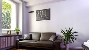 Ein modernes Wohnzimmer mit einem dunkelbraunen Ledersofa, einem Heizkörper, einem Blumentopf und einem gerahmten Bild an der Wand.