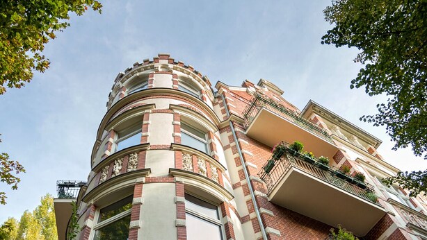 Ein mehrstöckiges Gebäude mit einer gewölbten Fassade, Balkonen mit Geländern und blauem Himmel.