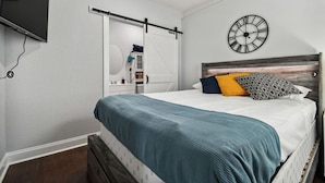 Een slaapkamer met een bed, een wandklok, een televisie en een schuifdeurkast.
