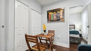 Een eetgedeelte met een houten tafel en stoelen, een schilderij aan de muur, en een deur naar een andere kamer.