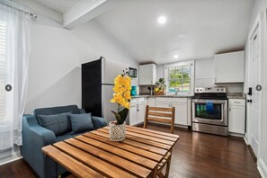 Un espace de vie compact comprenant un coin cuisine, un espace repas avec une table en bois, un canapé et une plante en pot.