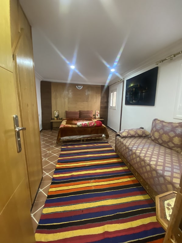 A bedroom with a bed, a sofa, a colorful striped rug, and a wooden wardrobe.