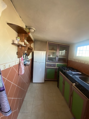 Eine kleine Küche mit Kühlschrank, Gasherd und Fenster.