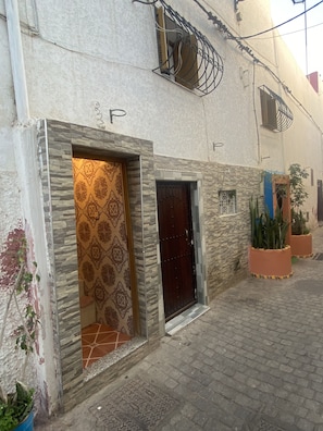 Ein Gebäude mit einer Tür mit Muster, einer steinernen Fassade und einem kleinen Fenster mit Gitter.