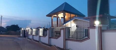 A gated residential area with a house featuring a covered porch and a water tank.