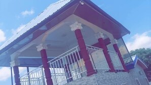 Un edificio de dos pisos con un balcón en el nivel superior, que cuenta con barandal de metal y cerramiento de vidrio.
