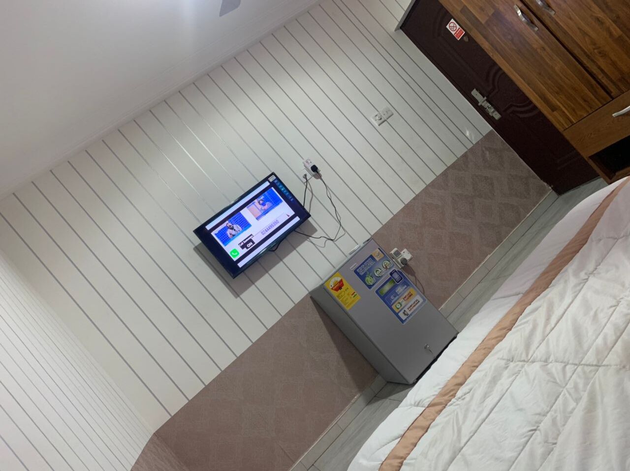 Ein Zimmer mit einem Bett, einem an der Wand befestigten Fernseher und einem kleinen Kühlschrank.