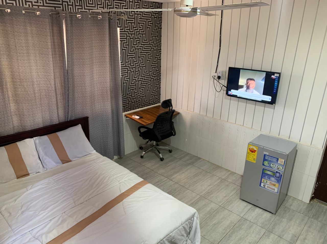 Una habitación de hotel con cama, escritorio, silla, televisión y refrigerador.