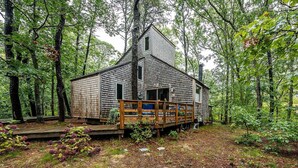 A rustic cabin with a wooden deck, surrounded by dense forest. - Welcome to Wellfleet! Classically Modern, Woodsy and Serene. (Wellfleet)