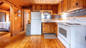A wooden cabin interior with a kitchen area, including a refrigerator, stove, and wooden cabinets. - Welcome to Wellfleet! Classically Modern, Woodsy and Serene. (Wellfleet)