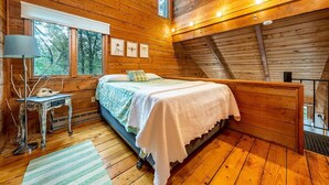 A wooden cabin bedroom with a bed, a small table with a lamp, and framed pictures on the wall. - Welcome to Wellfleet! Classically Modern, Woodsy and Serene. (Wellfleet)