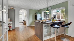A modern kitchen with a central island, bar stools, and a view of the outdoors through a window. - Beautiful home in Højby with WiFi (Højby)
