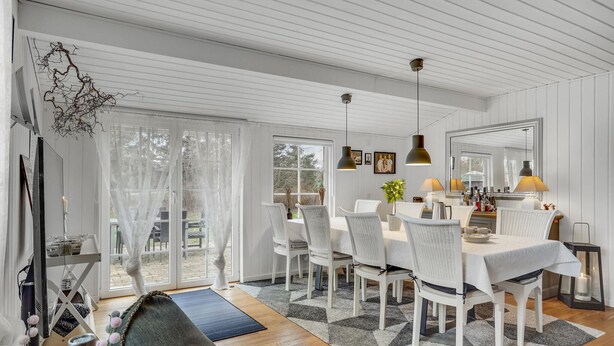 A dining area with a white table, wicker chairs, and a chandelier. There is a large window with a view of the outdoors. - Beautiful home in Højby with WiFi (Højby)