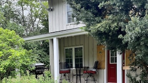Et toetagers hus med en veranda, en rød dør og en stensti, der fører til et siddeområde med to stole og et bord.