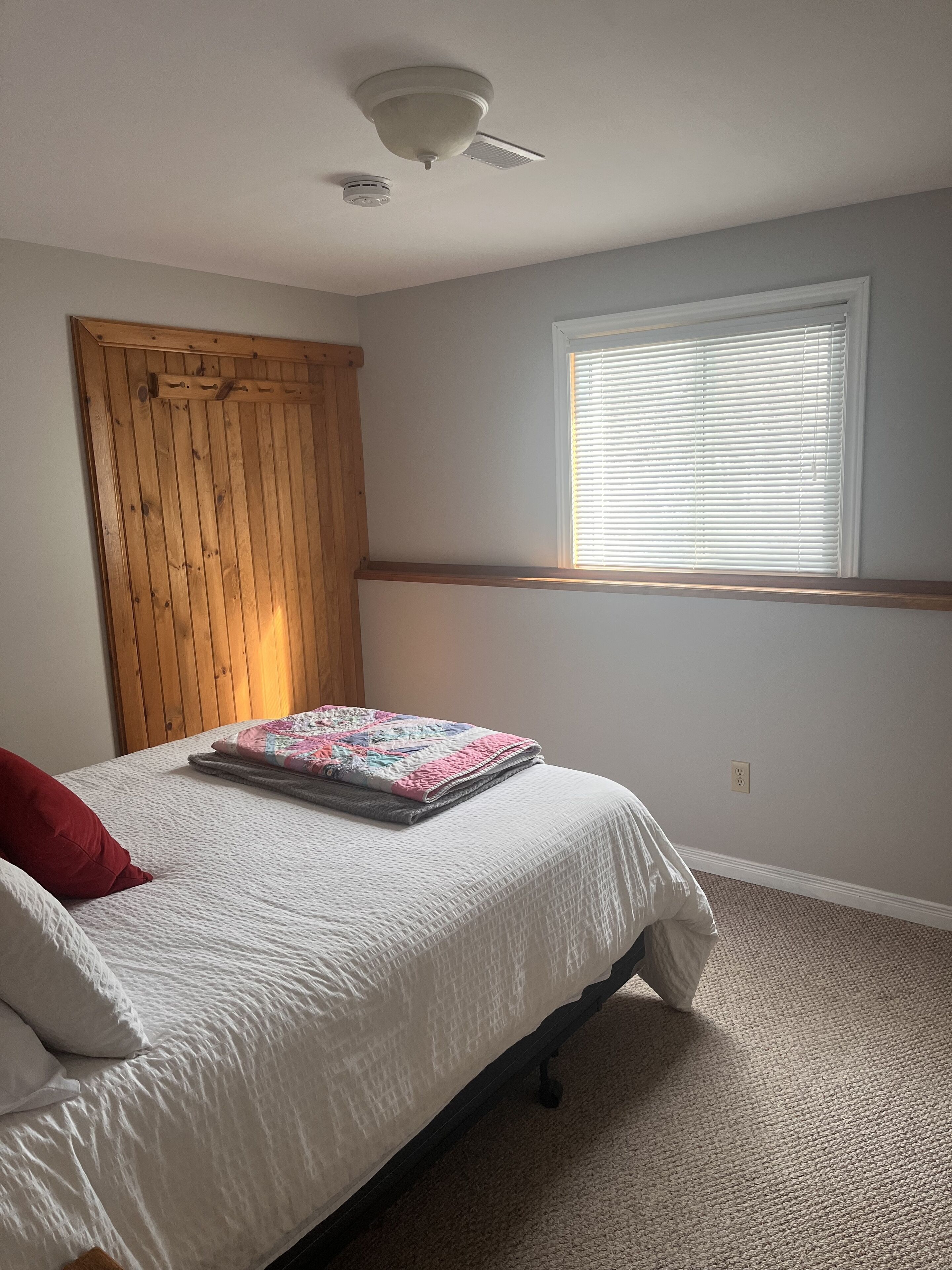 Un dormitorio con una cama, una ventana con persianas, un ventilador de techo y una puerta de madera.