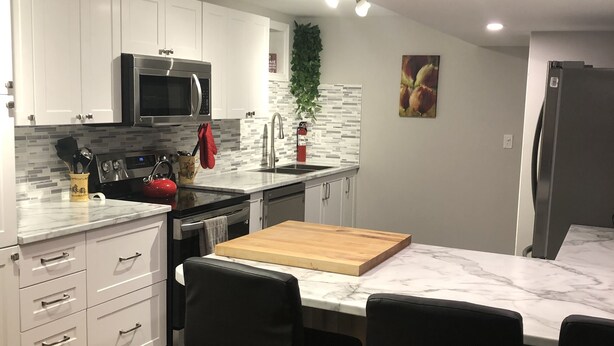 Et moderne køkken med hvide skabe, en stålfarvet mikroovn, en træø med barstole og et flisebeklædt backsplash.