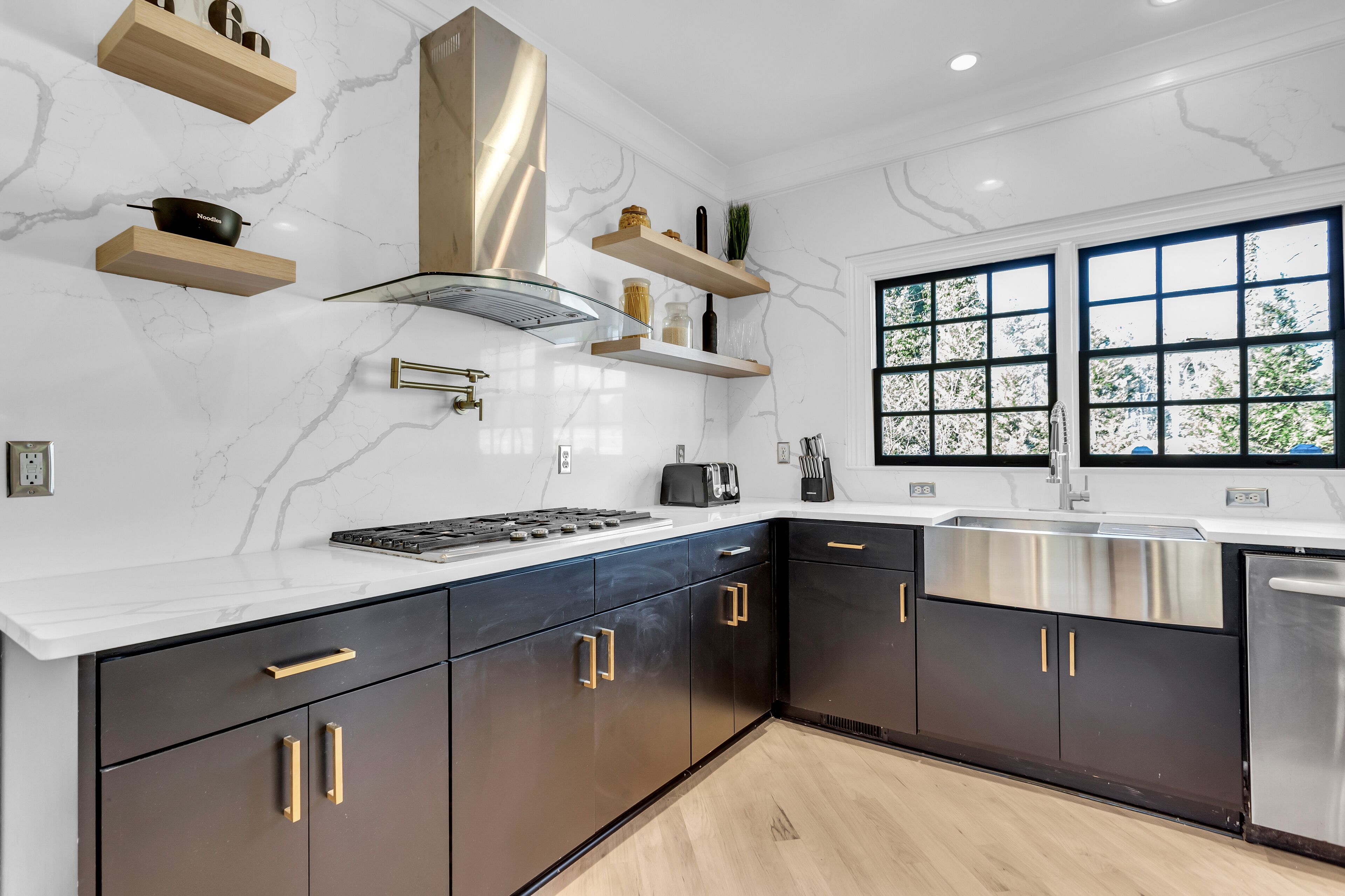 Een moderne keuken met donkere kastjes, een roestvrijstalen spoelbak en een raam met uitzicht op groen.