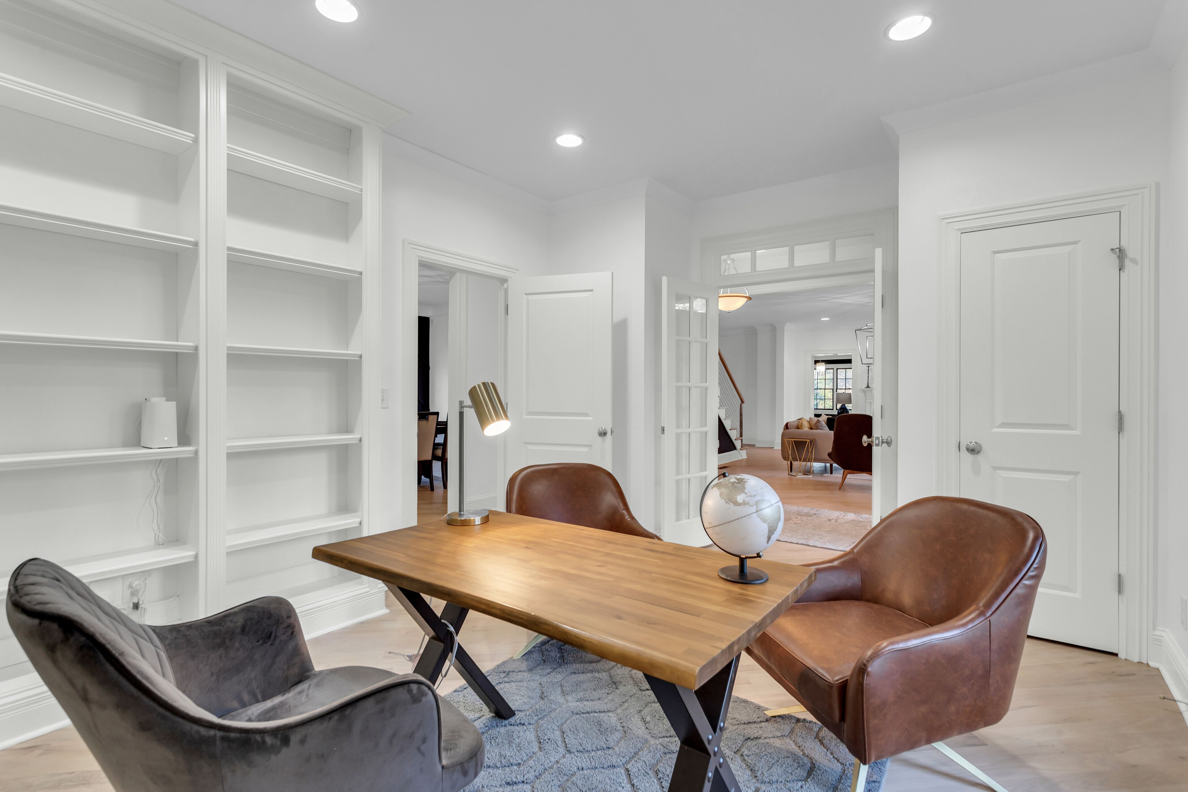 Une pièce moderne avec une table en bois, deux fauteuils en cuir, un globe terrestre et des étagères blanches.