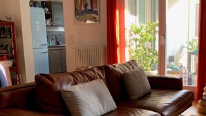 A brown leather sofa with cushions, a patterned rug, and a view of a kitchen and outdoor area through a glass door. - Presbyterian House with Terrace - Via Farini Isola (Milano)