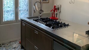 A kitchen with a gas stove, stainless steel cabinets, a window with patterned curtains, and a red appliance. - Presbyterian House with Terrace - Via Farini Isola (Milano)