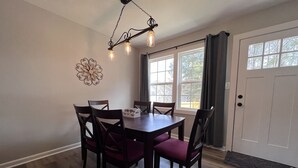 Un comedor con mesa de madera y cuatro sillas, un adorno en la pared y una ventana con cortinas.