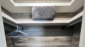 Un espacio de almacenamiento pequeño con suelo de madera, un tendedero metálico y un estante de piedra.