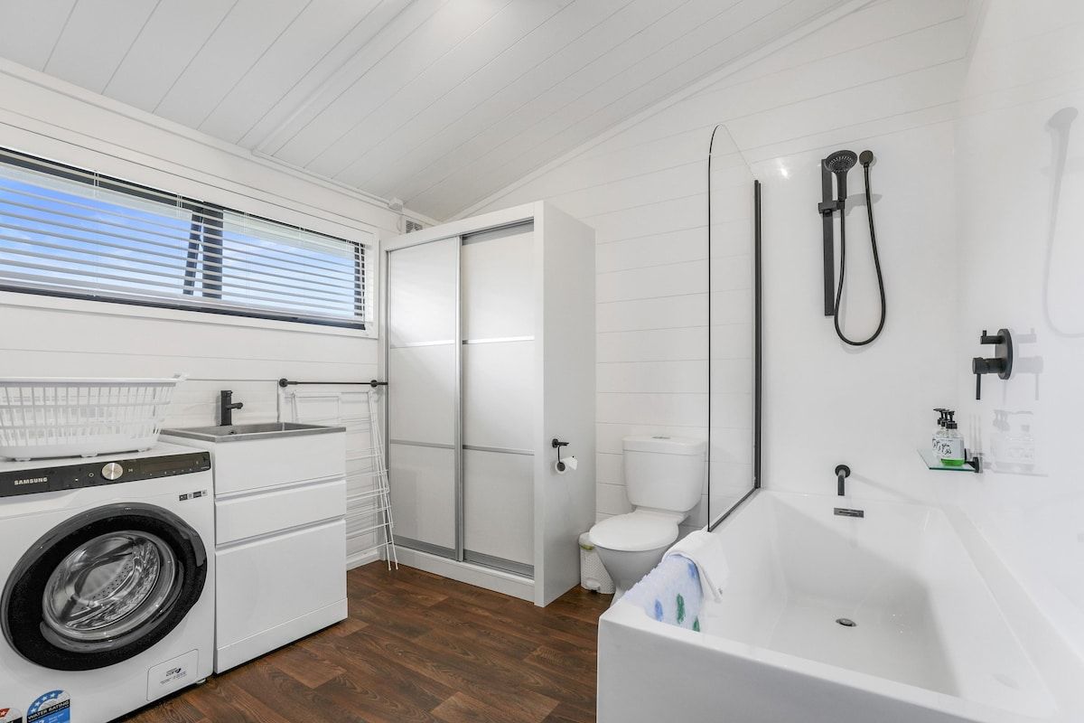 A compact, modern bathroom with a built-in washing machine, a shower, and a bathtub.