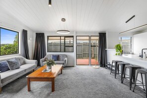 A modern living room with a sofa, coffee table, and a dining area with bar stools. - Be Rude Not To - Walk to Redwoods, Sleeps 7 (Rotorua)