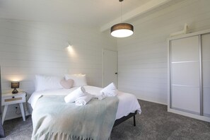 A hotel room with a bed, bedside table, lamp, and a wardrobe. - Be Rude Not To - Walk to Redwoods, Sleeps 7 (Rotorua)