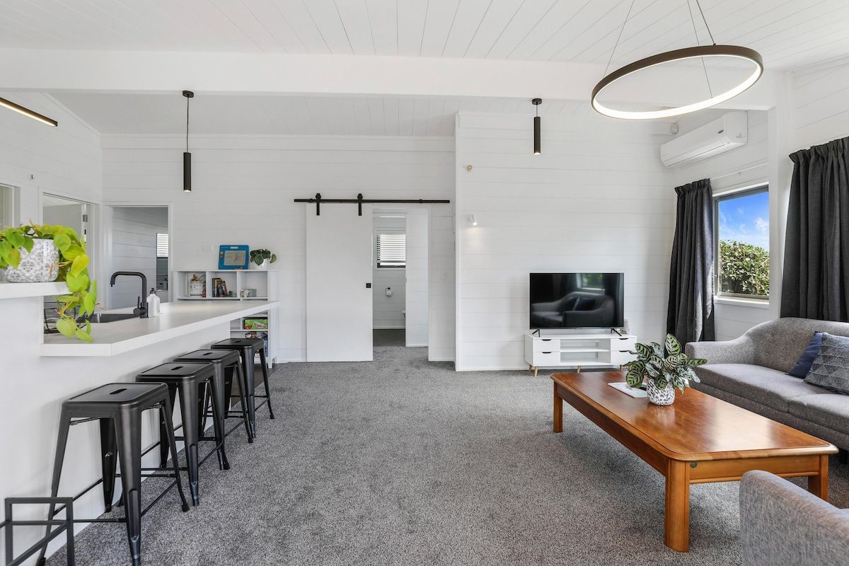 A modern living room with a sofa, a coffee table, a TV, and a kitchen area with bar stools.