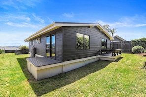 A modern two-story house with a deck, large windows, and a well-maintained lawn. - Be Rude Not To - Walk to Redwoods, Sleeps 7 (Rotorua)