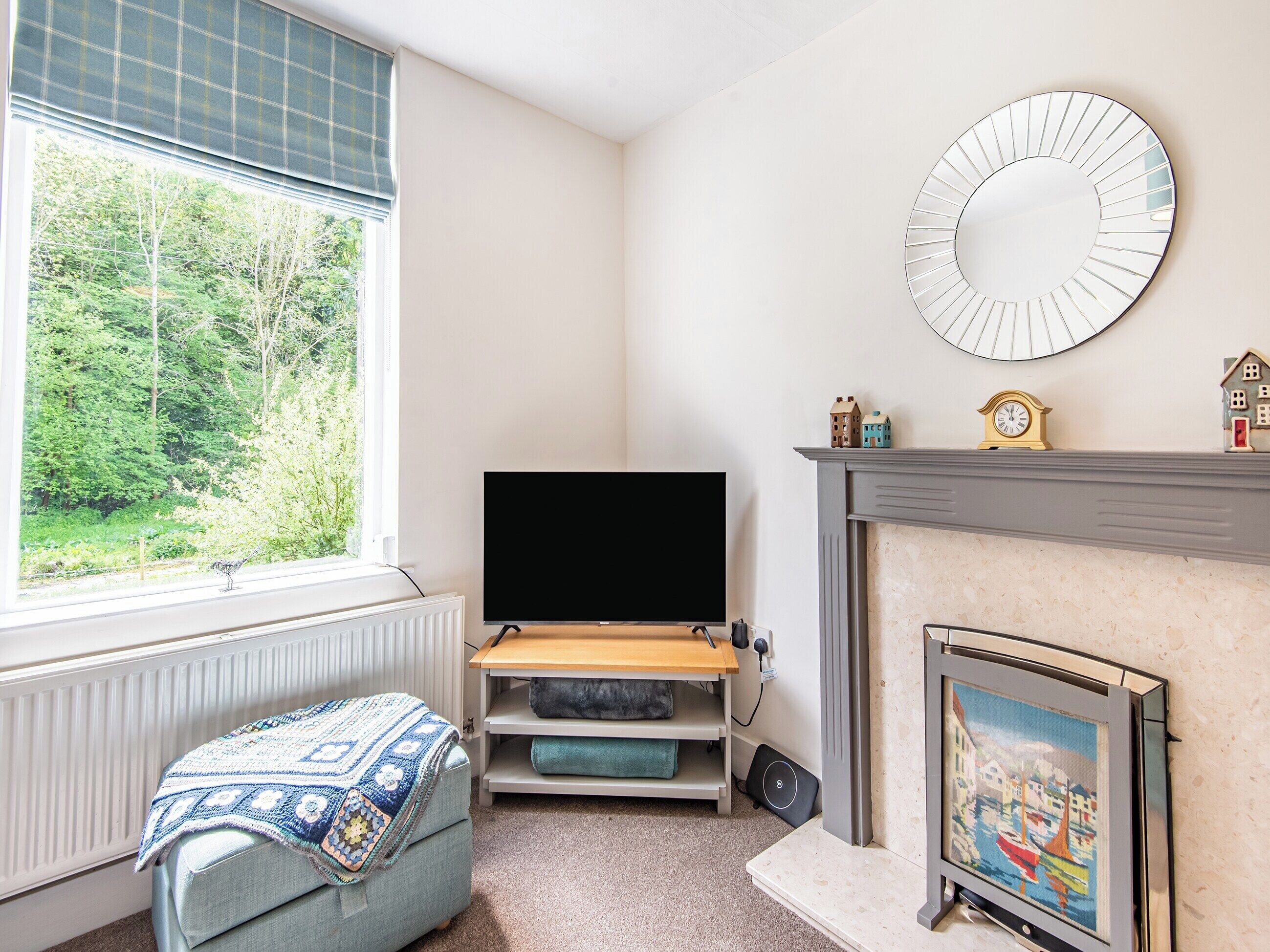 A living room with a TV, fireplace, and a window with a view of greenery.
