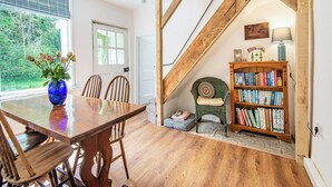 A dining area with a wooden table and chairs, a blue vase with flowers, and a bookshelf with books.