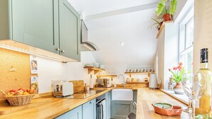 A compact kitchen with a wooden countertop, a built-in oven, and a sink. There are potted plants and a wine bottle on the counter.