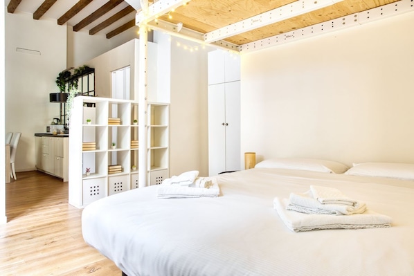 A bedroom with a large bed, a desk with a chair, and a shelving unit.