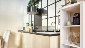 Ett kök med vita skåp, en svart bänkskiva, en diskho, en kaffebryggare och en hylla med vinglas.