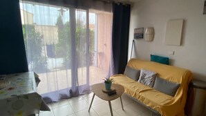 Ein Wohnzimmer mit einer Couch, einem kleinen Tisch und Blick durch eine Schiebetür auf einen Außenbereich.