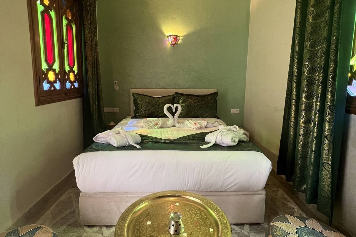 A room with a bed, a wall-mounted light fixture, a decorative wall piece, and a small table with a decorative item.