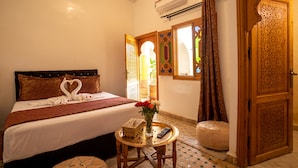 A hotel room with a bed, a small table with a vase of flowers, a remote control, and a decorative door. - Riad La Petite Rose (Marrakech)