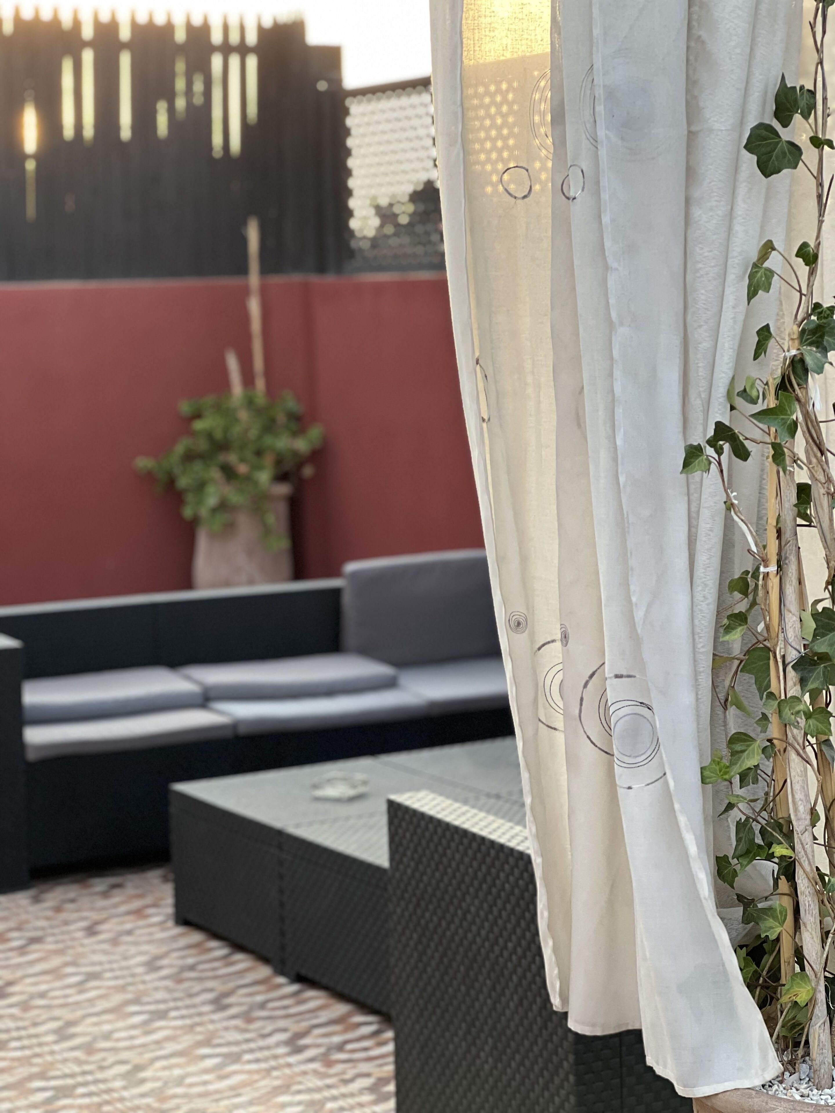 Een terras met een bank, een tafel, een bloempot en een gordijn.